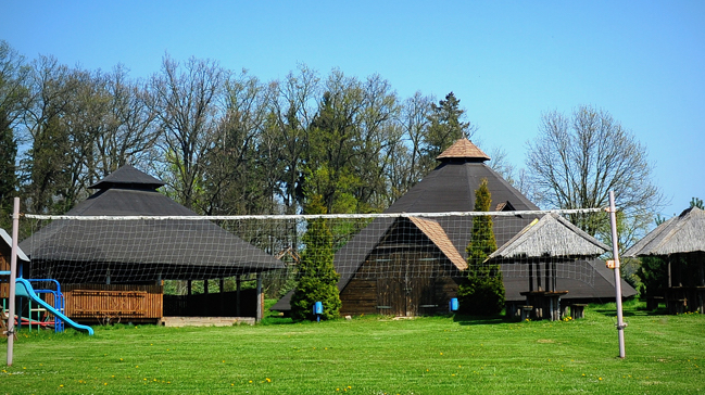 Wigwamy i zadaszone wiaty na trawiastym terenie zajazdu, obok siatka do siatkówki